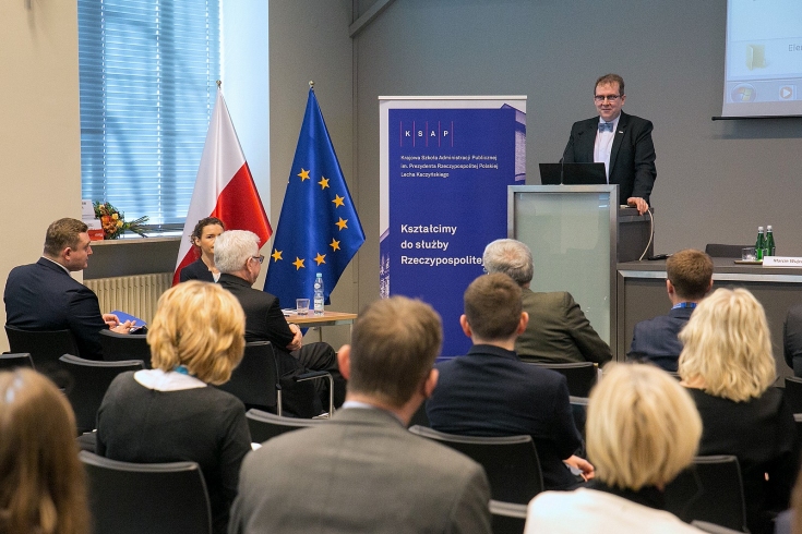 FOT. M. JASILEWICZ/MSZ Dyrektor KSAP Wojciech Federczyk przemawia z mównicy w auli KSAP. Widoczni siedzący uczestnicy konferencji. Obok mównicy baner KSAP i flagi polska i unijna.