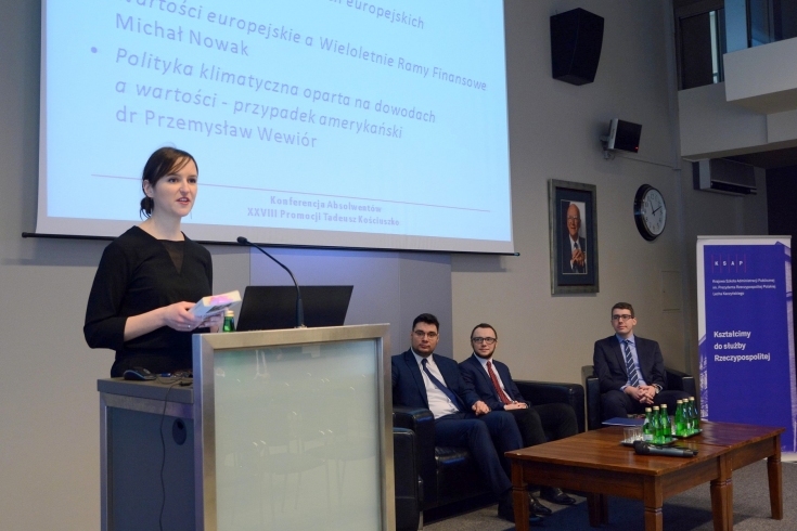 Prelegentka przy mównicy, w tle siedzą na fotelach pozostali prelegenci. Na ekranie wyświetla się prezentacja z tytułami wystąpień.